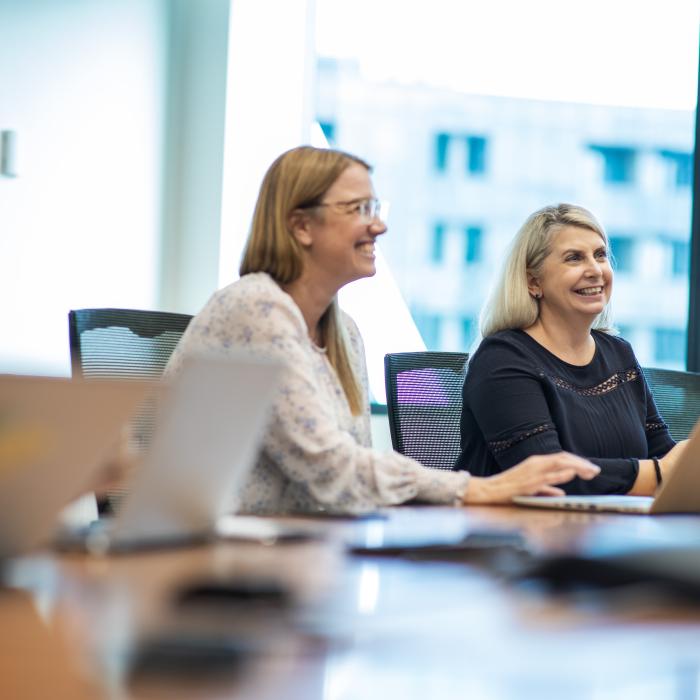 Two people smiling working on laptops